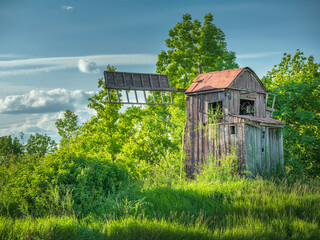 Abandoned wooden windmill in green bushes in spring day