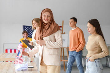 Voting Muslim woman near ballot box with USA flag at polling station