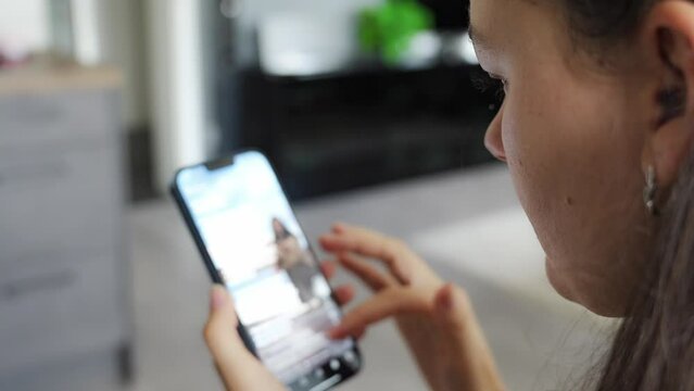 Young woman scrolls through her social media feed and watches a video while sitting at home.