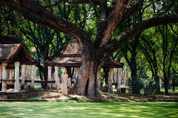 Young woman on the bank of Beautiful green pond in ancient park of Sukhothai, Thailand