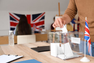 Voting young man near ballot box with UK flag at polling station, closeup