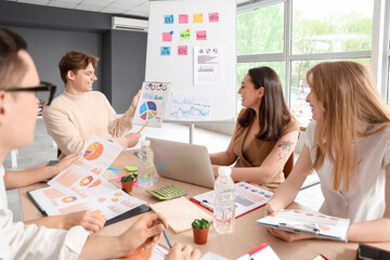 Young business man with diagrams and his colleagues working on marketing plan in office