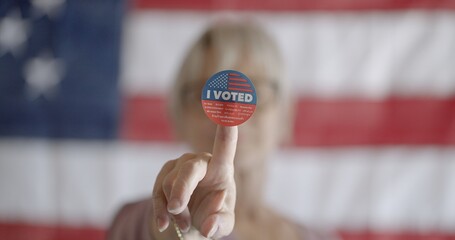 Elderly woman voter holds up sticker on finger, in front of her face. Close up, focus on sticker...