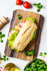 Ciabatta sandwich with lettuce, cheese, tomatoes and ham at cutting board. Fast food, snack or lunch.