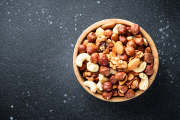 Nuts assortment at black background. Almond, hazelnut, cashew in wooden bowl. Flat lay with copy space.