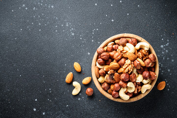 Nuts assortment at black background. Almond, hazelnut, cashew in wooden bowl. Flat lay with copy...