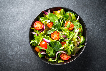 Green Salad with salad leaves and vegetables at black background. Top view with copy space.