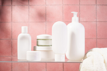 Cosmetic products at glass shelf at pink bathroom background.