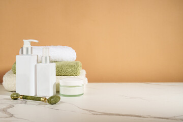 Skin care products in the bathroom. Face cream, serum bottle, jade roller and stack of towels.