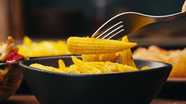 Close-up of fermented yellow mini corn with black pepper on black plate. Preservation of vegetables in glass jars. Fermentation preserved mini corns with spices.