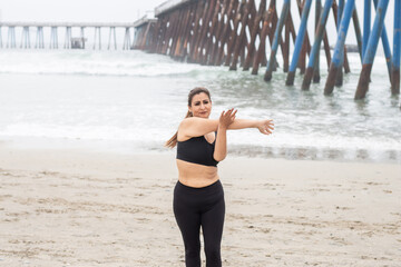 sporty, middle-aged latin woman warming up and stretching arms on the beach, mature Mexican fitness