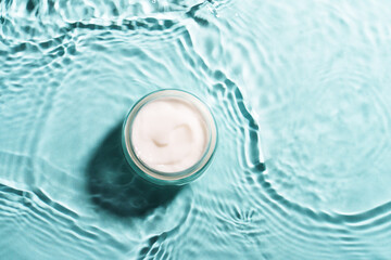 Cream jar in the water on blue background. Flat lay image.