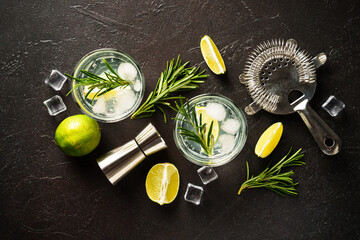 Gin tonic, traditional cocktail with gin, tonic, ice cubes, lime and rosemary on black background. Top view.