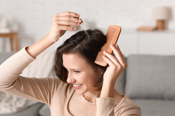 Naklejka premium Beautiful young happy woman using care products and brushing her short hair at home