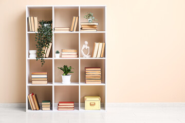 Fototapeta premium Modern shelving unit with books and home decor near beige wall