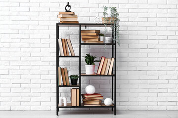 Modern shelving unit with books and home decor near white brick wall