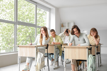 Students passing exam at desks in classroom
