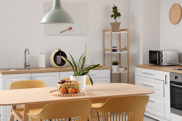 Interior of stylish kitchen with dining table, houseplant, fruits and lamp, closeup