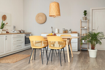 Interior of stylish kitchen with dining table, chairs, white counters and lamp