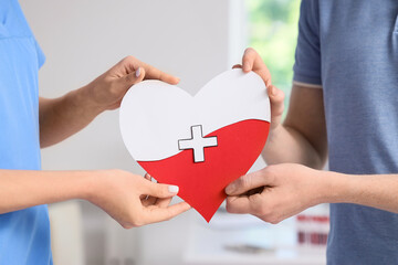 Male blood donor with nurse holding paper heart in clinic, closeup