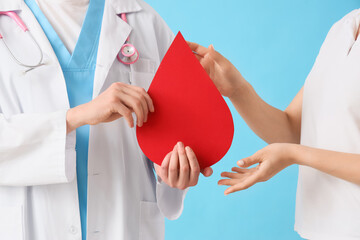 Male doctor giving paper blood drop to woman on blue background, closeup