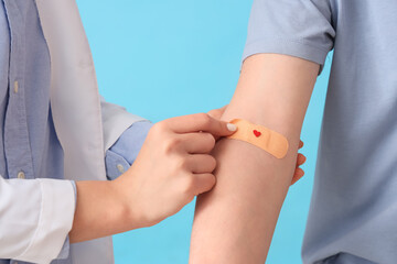 Female doctor applying patch on blood donor's arm on blue background, closeup