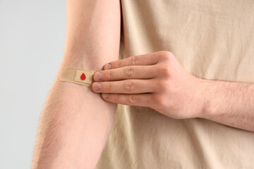 Male blood donor with applied patch on light background, closeup