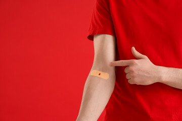 Male blood donor pointing at applied patch on red background, closeup
