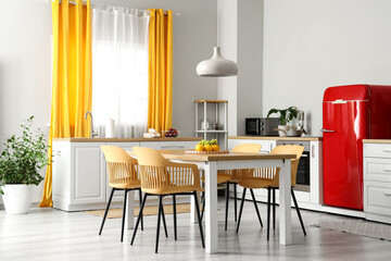 Interior of modern kitchen with white counters, dining table, red fridge, chairs and lamp