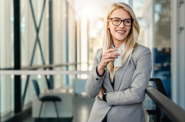 Obraz premium Experienced businesswoman standing with disposable coffee cup in a lobby of an office building.