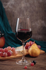 Glass of rich red wine served with cheese plate and fruits on dark wooden background. Appetizers table with wine glasses, rustic style table setting in winery