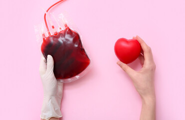 Female hands with blood pack and heart on pink background. World Blood Donor Day