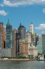 Obraz premium New York, NY, USA - August 1, 2023: Green tipped battery park authority building on shoreline with skyscraper collection in back under blue cloudscape, Some green trees