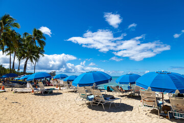 Tourists relaxing on chaise lounges with blue umbrellas in Waikiki Beach, Honolulu., Hawaii, USA