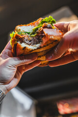 Close-up of hands holding a half-eaten burger with visible layers of bun, patty, and lettuce
