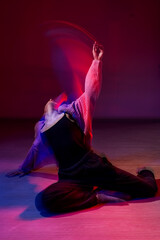 A young woman dances contemporary dances in blue and red light. Long exposure. Vertical photo. 