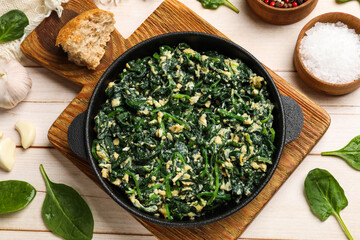 Tasty spinach dip with eggs in dish served on light wooden table, flat lay