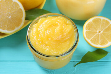 Delicious lemon curd in glass jar, fresh citrus fruit and green leaves on light blue wooden table, closeup