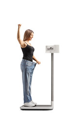 Happy young woman in a big sized jeans and weighing on a medical scale