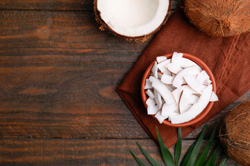 Coconut pieces in bowl, nuts and palm leaf on wooden table, top view. Space for text