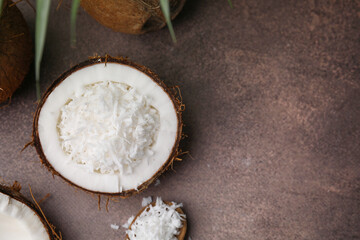 Coconut flakes in nut shell and spoon on brown table, flat lay. Space for text