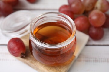 Wine vinegar in glass jar and grapes on light wooden table, closeup