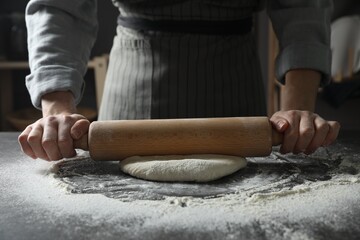 Woman rolling pizza dough with pin at table, closeup