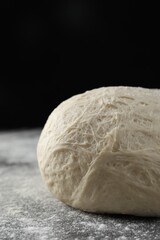 Raw homemade dough and flour on black table, closeup