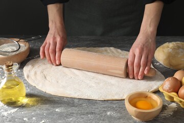 Woman rolling raw dough at grey table, closeup
