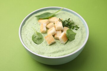 Delicious spinach cream soup with croutons in bowl on green background