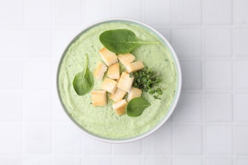 Delicious spinach cream soup with croutons in bowl on white tiled table, top view