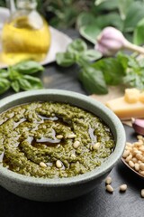 Tasty pesto sauce in bowl and pine nuts on black table, closeup