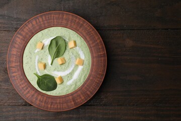 Delicious spinach cream soup with leaves and cheese in bowl on wooden table, top view. Space for text