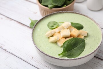 Delicious spinach cream soup with leaves and croutons in bowl on white wooden table, space for text